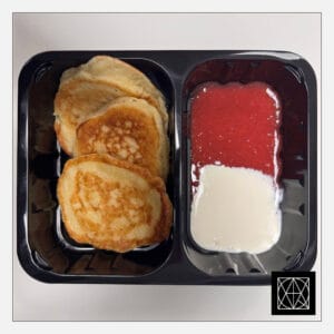 Mieliniai blynai, pateikiami su trintomis braškėmis ir grietine